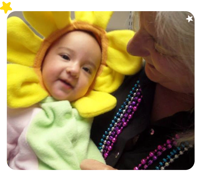 A woman holding a baby wearing a flower costume.