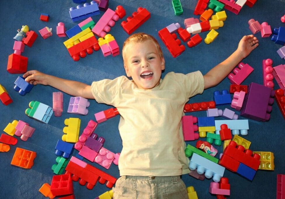 A boy laying on the ground with many colorful blocks.