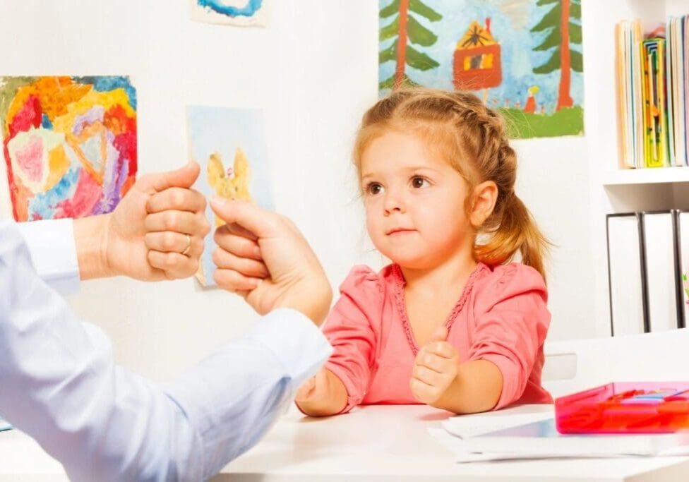 A little girl sitting at the table with an adult.